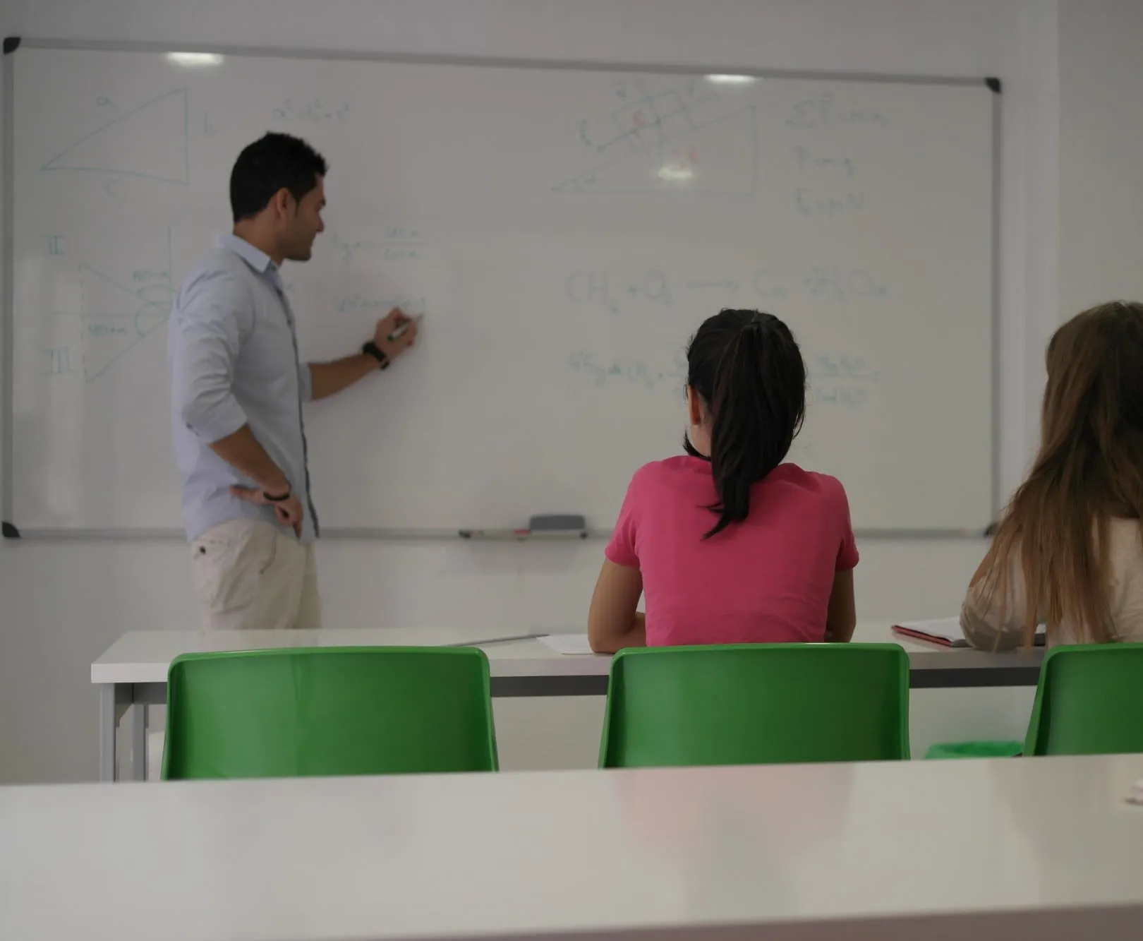 El profesor explica física y química en la pizarra a dos alumnas