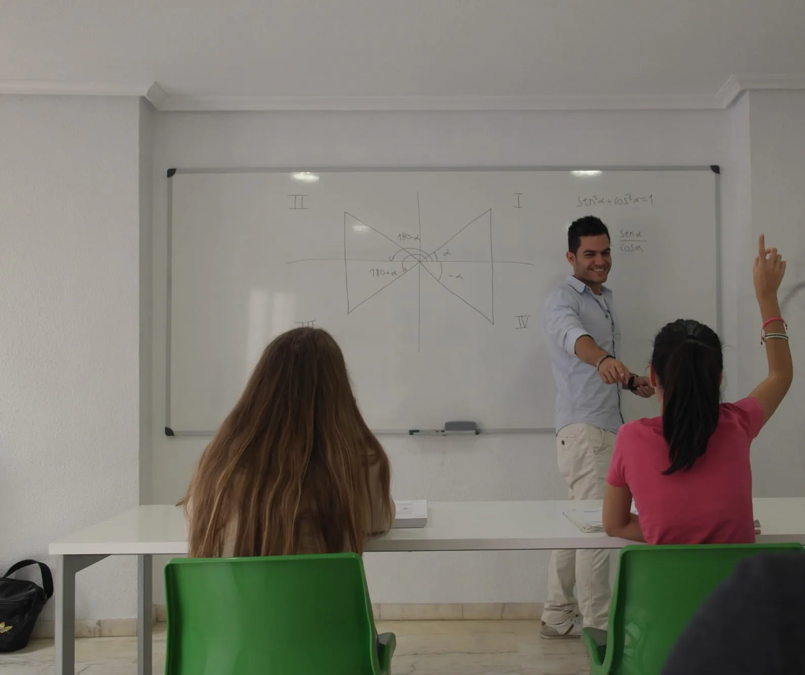 Una alumna levanta la mano para preguntar al profesor en la pizarra