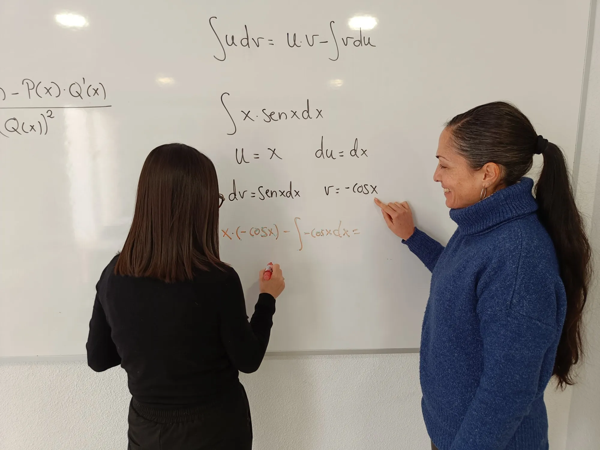 Una profesora ayuda a una alumna a resolver una integral en la pizarra